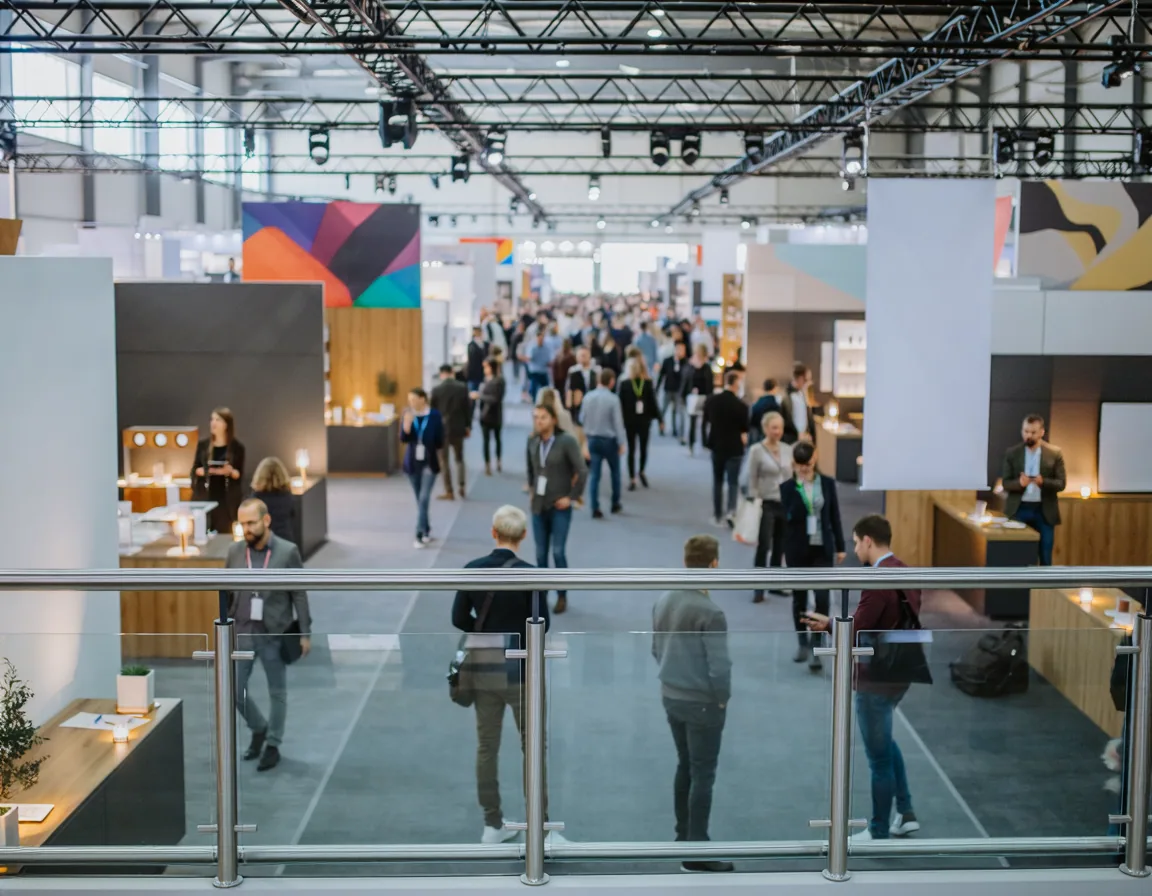 Busy exhibition hall aisle lined with booths, seen from a mezzanine